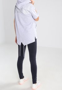 Light grey short-sleeve hoodie with a textured grey upper section, slightly longer back, paired with black skinny jeans and white sneakers.