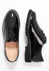 Czarne lakierowane buty na sznurówki z wzorem brogue, okrągłym noskiem, teksturowanymi akcentami oraz grubą gumową podeszwą zapewniającą przyczepność.
