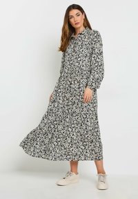 Langes, knopfbares Kleid mit einem dunklen Blumenmuster, locker sitzend, mit langen Ärmeln, gerafftem Bund und einem fließenden Rock, kombiniert mit hellen Sneakers.