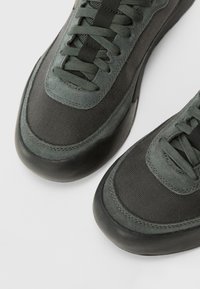 Mørk grønne sneakers med en blanding af mesh og ruskind, rund gummisål, stikninger og flade snørebånd.