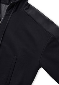 Sudadera negra con cremallera frontal, con una textura de tejido suave en el hombro y un bolsillo delantero, que enfatiza un diseño minimalista.