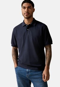 Marineblå polo skjorte lavet af struktureret stof med knaplukning, korte ærmer og klassisk krave, båret med blå jeans.