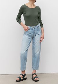 Grüner Langarm-Body, hellblaue gerade Jeans mit Fronttaschen und dunkelgrüne Plateausandalen mit dicker Sohle.