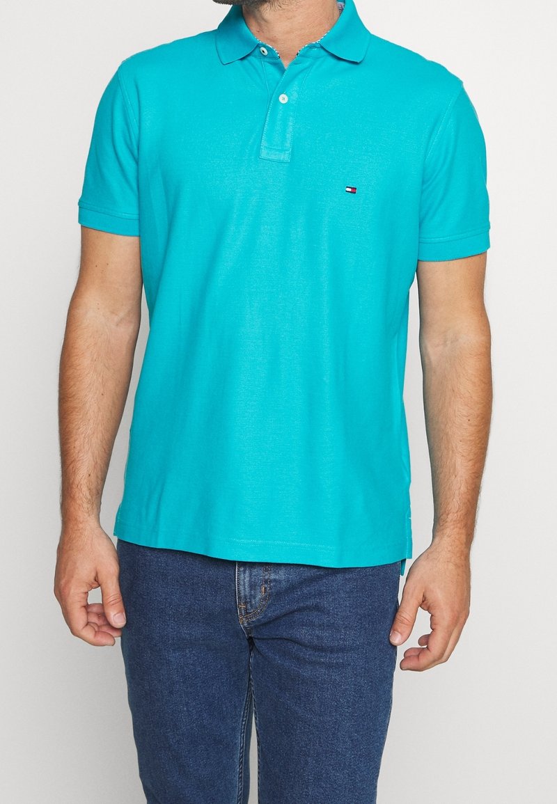 Polo turquoise avec col, patte à trois boutons et manches courtes. Tissu doux, détail logo discret, associé à un jean bleu.