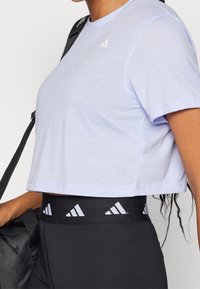 Camiseta deportiva corta de color púrpura claro con mangas cortas y un logotipo blanco. Usada con leggings negros que tienen una cintura de marca.