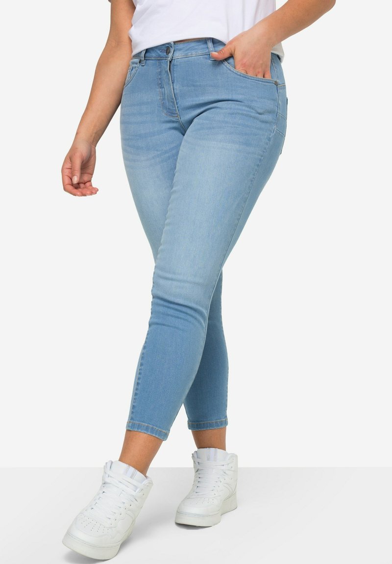 Světlé modré džíny skinny s středním pasem, předními kapsami a zkráceným lemem, doplněné bílými vysokými teniskami.