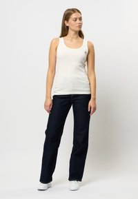 Vitt ribbat linne med rund halsringning och liten logotyp, matchat med mörkblå vida jeans och vita sneakers. Enkelt, avslappnat outfit.