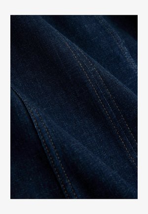 Mørkeblåt denimstof med en subtil tekstur og gyldengule syninger. Materialet har en glat finish med små tonevariationer.