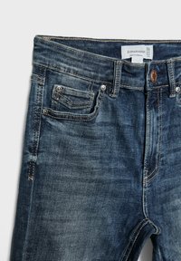 Tamne traperice tamnoplave boje s izblijedjelim završetkom. Značajke uključuju zatvarač, stil s pet džepova i kontrastne šavove. Vidljiva oznaka veličine.