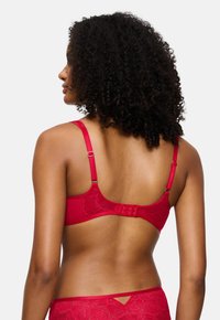 Sutiã de renda vermelha com alças ajustáveis, fecho de gancho e olho, e padrão floral, exibindo uma textura suave e um design estruturado.