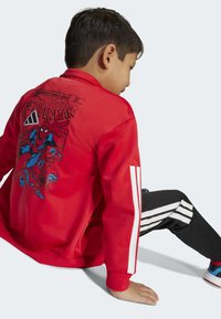 Rode jas met een Spider-Man graphic op de achterkant, witte Adidas strepen op de mouwen, geribbelde manchetten, gecombineerd met zwarte broek met witte strepen.