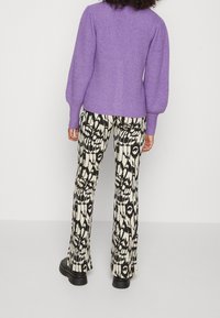 Suéter de punto púrpura con mangas abullonadas, combinado con pantalones acampanados negros y crema con un atrevido diseño abstracto.