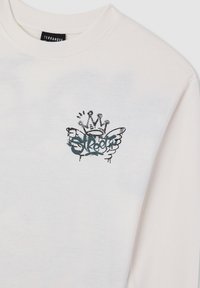 Biała koszula z długim rękawem, z małym, czarno-niebieskim graffitowym wzorem przedstawiającym koronę, skrzydła oraz słowo "Street" na klatce piersiowej.