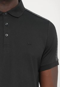 Čierne polo tričko s trojčiarkovým zapínaním, rebrovaným golierom a jemne embosovaným logom na hrudníku; má textúrované rukávy.