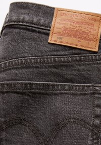 Jeans in denim nero con un'etichetta in pelle. L'etichetta presenta il testo in rilievo "Levi Strauss & Co." e un design di cavalli. Taglio classico 501®.