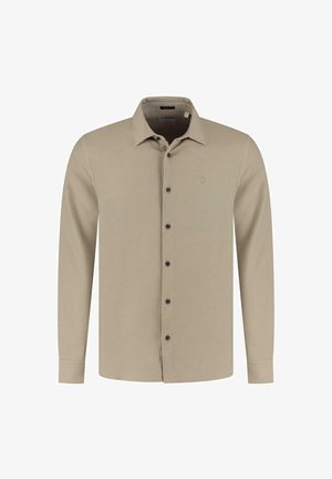 Vaalean beige pitkähihaisessa nappipaidassa on kaulus ja mustat napit, esitetty tasaisesti valkoista taustaa vasten.