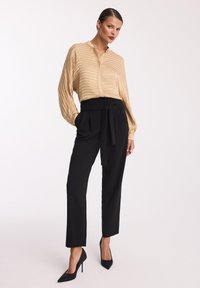 Beżowa bluzka w paski z długimi rękawami i kołnierzykiem, połączona z czarnymi spodniami z wysokim stanem z paskiem. Czarne, szpiczaste szpilki.