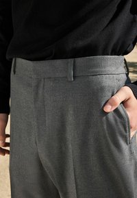 Szare dopasowane spodnie o gładkiej teksturze, z płaskim przodem, bocznymi kieszeniami oraz zamkiem z zapięciem na guzik.