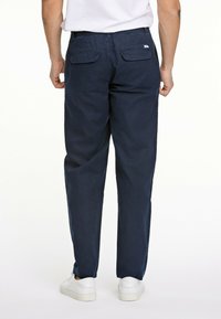 Pantalones azul marino de corte relajado, con bolsillos en la parte trasera y una textura suave, combinados con zapatillas blancas.