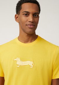 Geel katoenen t-shirt met een geborduurde gestreepte teckel in wit en geel. Korte mouwen, ronde hals, gladde textuur.