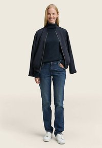 Navy bomber jacket with a zip front, turtleneck top, blue jeans, and white sneakers. Smooth fabric, relaxed fit, and simple design.