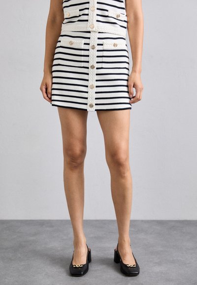 Stripet miniskirt i hvid og marineblå, med guldknapper, to forlommer og en tekstureret taljedetalje. Båret med sorte blokhælsko.