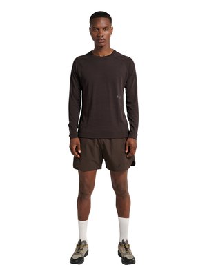 Mand stående iført en sort langærmet trøje, mørkebrune shorts, hvide sokker og beige og sorte vandresko på en hvid baggrund.