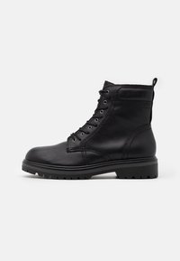 Botines de cuero negro hasta el tobillo con puntera redonda, cordones en la parte delantera y suela resistente. Presentan detalles de costura y una tira en la parte posterior.