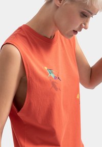 T-shirt sans manches en coton orange avec des figures colorées brodées. Encolure ronde et ouvertures latérales pour un ajustement décontracté.