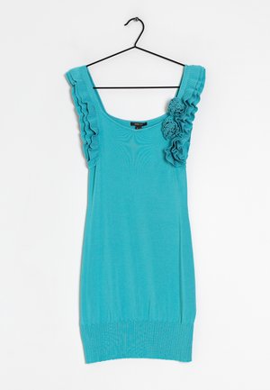 Robe turquoise sans manches avec bretelles volantées et deux détails de fleurs en tissu sur l’épaule droite, suspendue à un cintre noir.