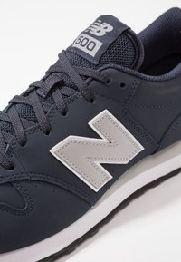 Zapatilla de navy con parte superior sintética, lengua de malla texturizada, prominente logo gris "N" y entresuela blanca con una suela de goma negra.