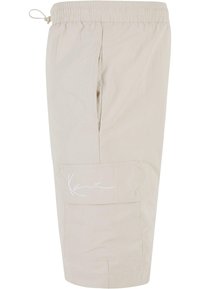 Beige cargo shorts med elastisk livlinje, sidelomme og en fremtredende hvit signatur brodert på siden, laget av lett materiale.