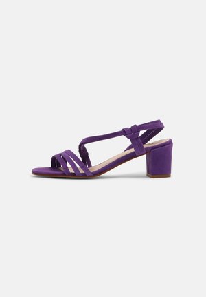 Sandale à talon en daim violet avec bout ouvert, présentant plusieurs brides croisées, une bride arrière et un talon bloc pour la stabilité.