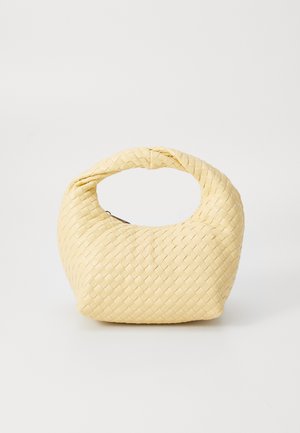 Petit sac à main tissé jaune pâle avec poignée circulaire et fermeture éclair, présenté sur un fond blanc uni.