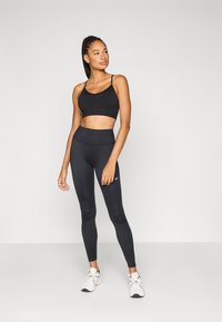 Μαύρο αθλητικό crop top και ψηλόμεσο κολάν, κατασκευασμένα από λεία ύφασμα. Διαθέτουν διακριτική λεπτομέρεια με λογότυπο στο κολάν.