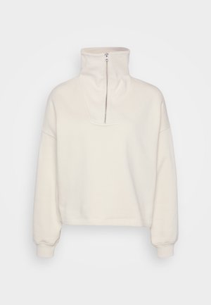 Cremfarbener Fleece-Pullover mit hohem Kragen und halbem Reißverschluss. Das Design umfasst locker fallende Ärmel und einen verkürzten Saum.