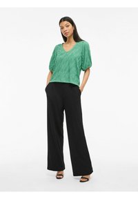 Top plissettato verde con scollatura a V e maniche corte a sbuffo, abbinato a pantaloni neri a gamba larga. Tessuto liscio con design testurizzato.