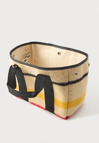 Ορθογώνια μπεζ τσάντα από πίλημα με μαύρες, κίτρινες και κόκκινες ρίγες, μαύρους χειροκράτες, κουμπιά ασφαλείας και ανοιχτή κορυφή που δείχνει την εσωτερική ετικέτα.