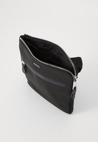 Schwarze Nylon-Tasche mit einem Reißverschluss oben, ausgestattet mit einer glatten Fronttasche, silberner Hardware und einem verstellbaren Riemen. Das Innere ist mit schwarzem Stoff ausgekleidet.