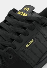 Czarne sneakersy z teksturowanej skóry, z żółtym logo "GLOBE", płaskimi czarnymi sznurowadłami i szczegółami przeszycia. Okrągły fason noska.