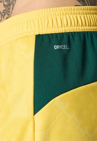 Guleid sportsbukser med en teksturert overflate og mørkegrønn sidepanel. Inkluderer "DRYCELL" merke nær midjebåndet.