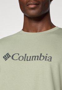 Light green cotton t-shirt featuring a large dark gray "Columbia" logo across the chest, with a crew neck and short sleeves.