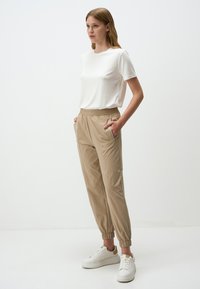 Beige elastische taillebroek met zijzakken, gecombineerd met een witte T-shirt met korte mouwen. Witte sneakers maken de outfit af.