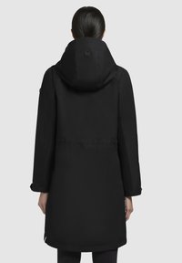 Zwarte geïsoleerde jas met een grote capuchon, lange mouwen en verstelbare manchetten. Bevat een tailleband en een logo op de capuchon. Gladde textuur.