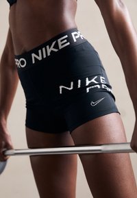 Czarne szorty Nike Pro z białym logo i nazwą marki na pasku oraz udzie. Materiał wydaje się elastyczny i dopasowany, o gładkiej fakturze.
