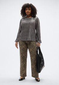 Szürke pliszírozott hosszú ujjú felső barna és fekete zebra csíkos nadrággal párosítva. Fekete, mintás kézitáska és fekete cipők.