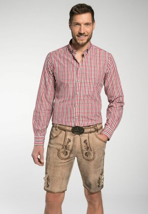 Ein rot-weiß karierter Langarmshirt kombiniert mit hellbraunen Ledershorts, die mit floralen Stickereien und einer dekorativen Gürtelschnalle verziert sind.