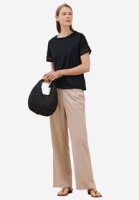 Maglietta nera a maniche corte con dettagli in pizzo, pantaloni beige a gamba larga e una borsa intrecciata nera texture. Sandali semplici completano l'outfit.