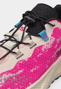 Κοντινή λήψη ροζ και λευκού παπουτσιού για τρέξιμο με μαύρες ελαστικές κορδόνια και μπλε θηλιές κορδονιών σε υφή σόλας.