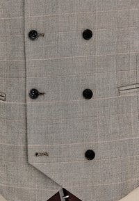 Dwurzędowa szara marynarka w kratę z sześcioma czarnymi guzikami i dwoma poziomymi, wszywanymi kieszeniami widocznymi z przodu.